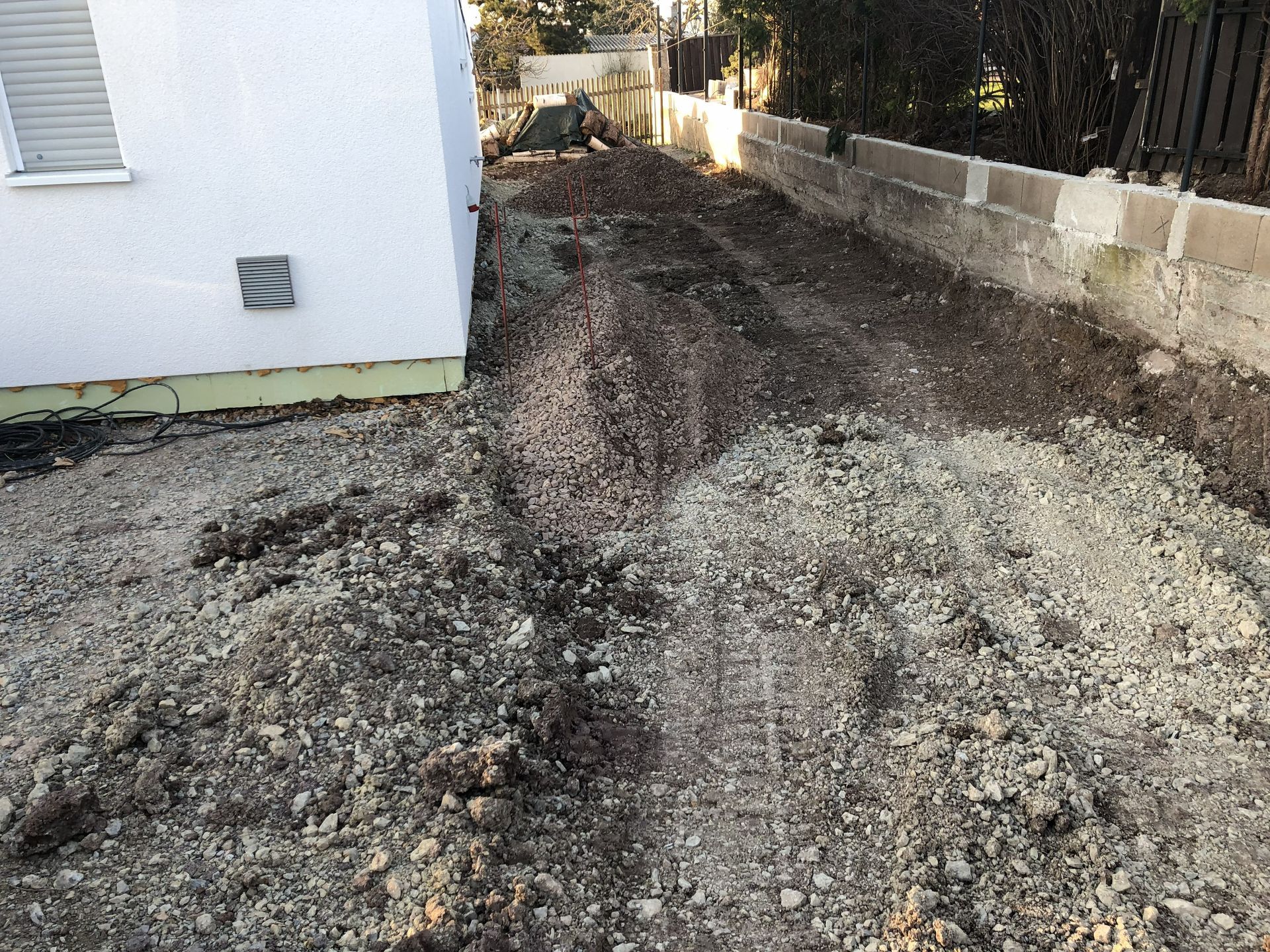 Eine Kiesauffahrt neben einem weißen Gebäude und einer Betonmauer, mit schlammigen Reifenspuren und ohne Menschen.