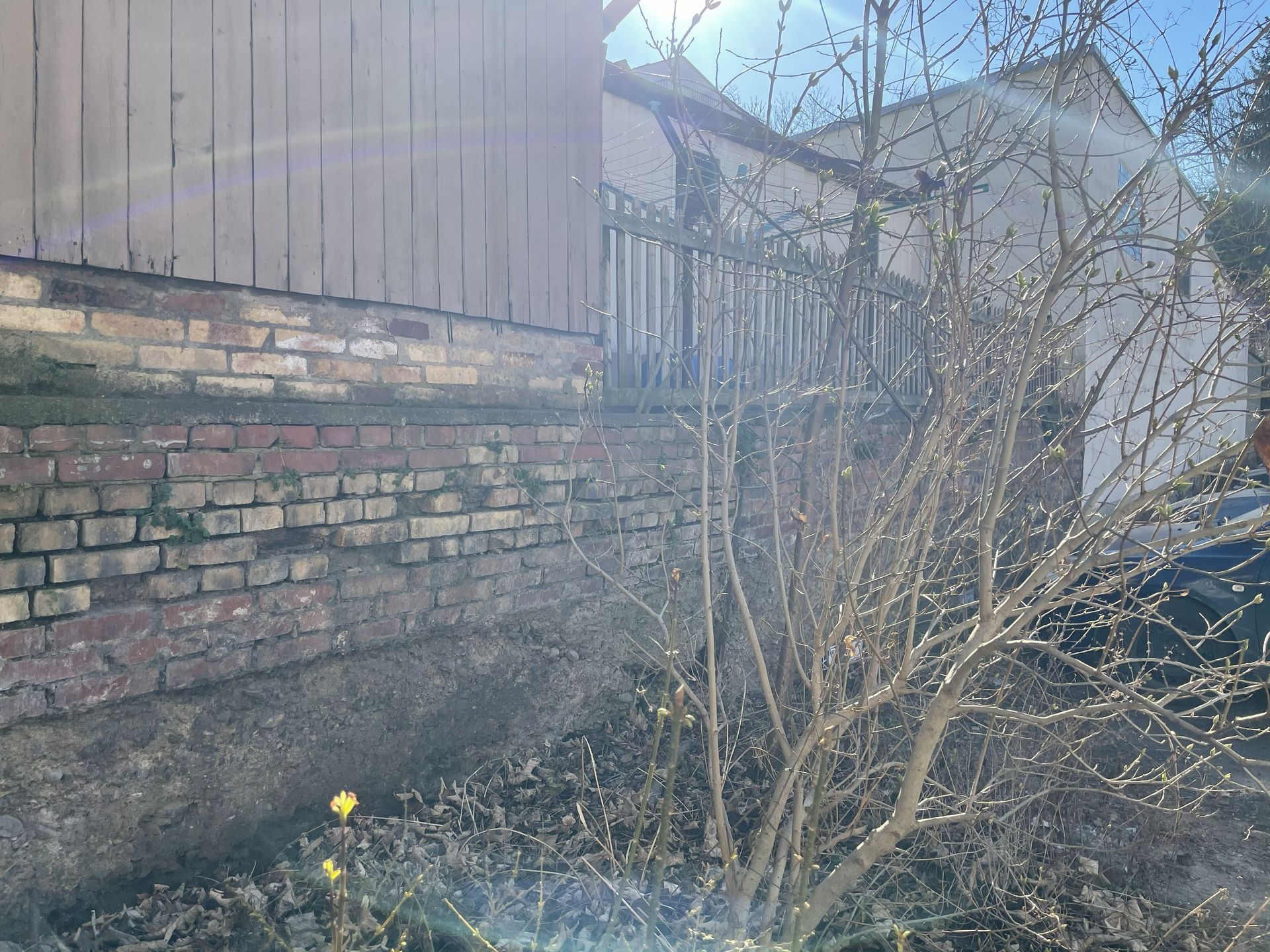 Hinterhof mit Backsteinmauer, kahlen Sträuchern und Holzzaun im sanften Tageslicht
