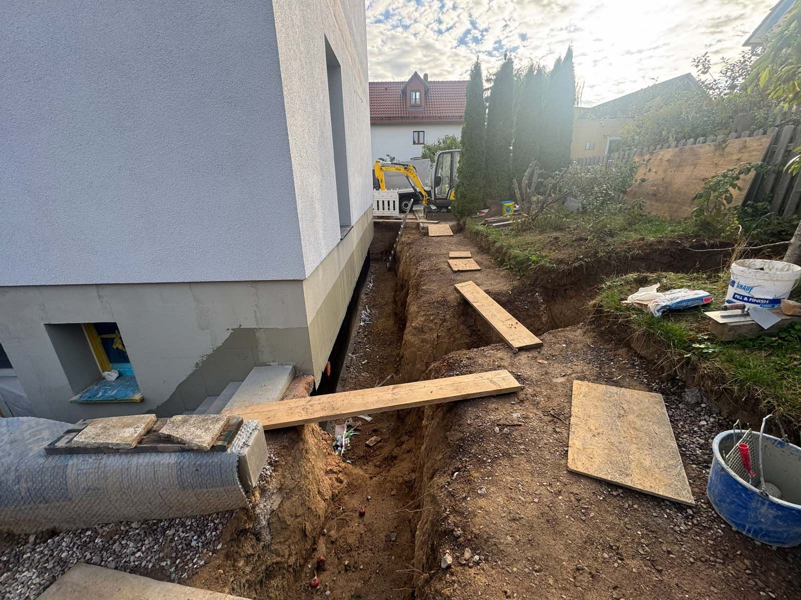 Ein schmaler Erdgraben neben einem Haus, über den im Hinterhof provisorische Holzplanken als Gehweg verlaufen.