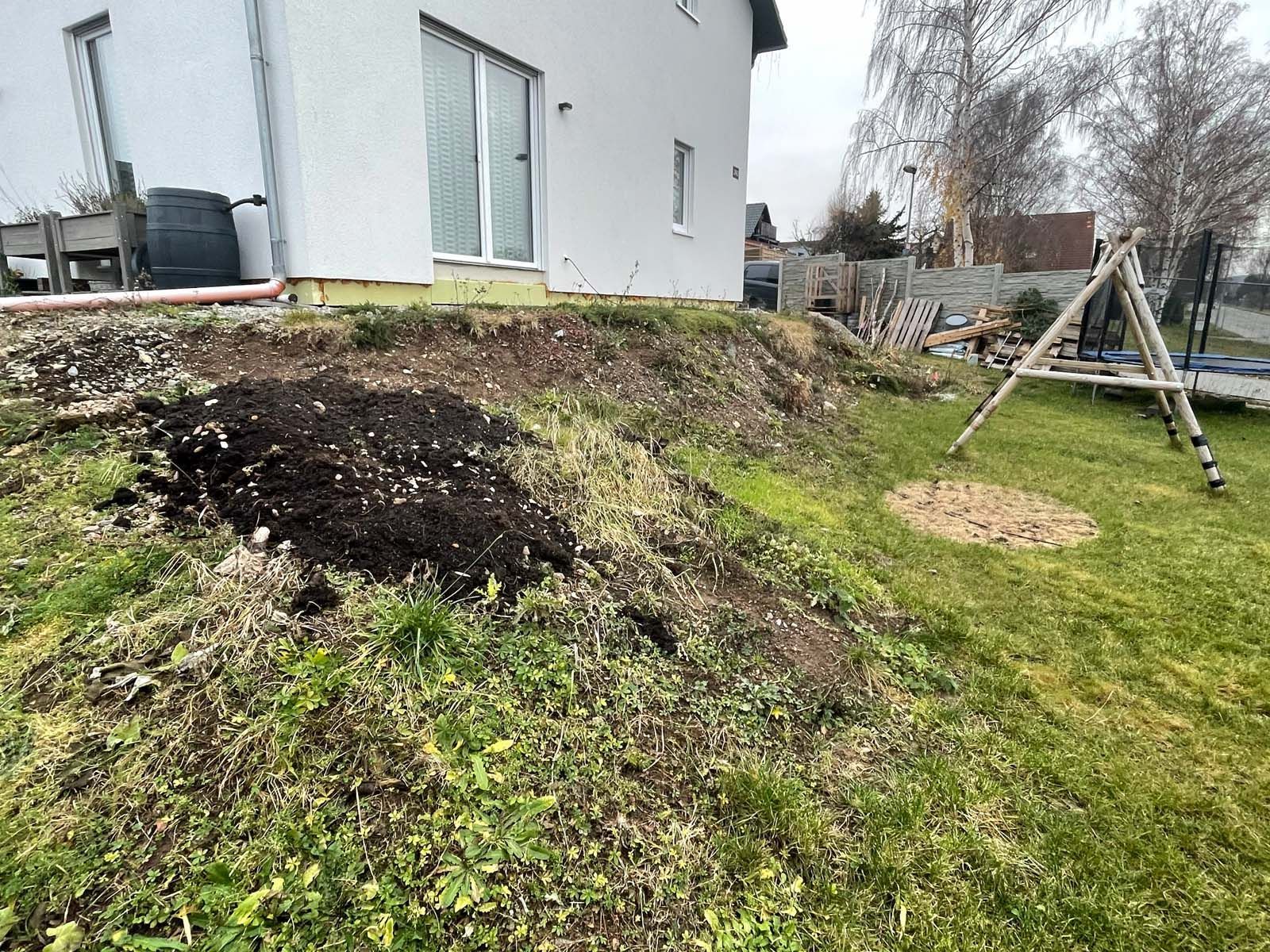 Hinterhofhang mit freiliegendem Boden, einem grauen Haus und einer hölzernen Schaukel auf dem Rasen.