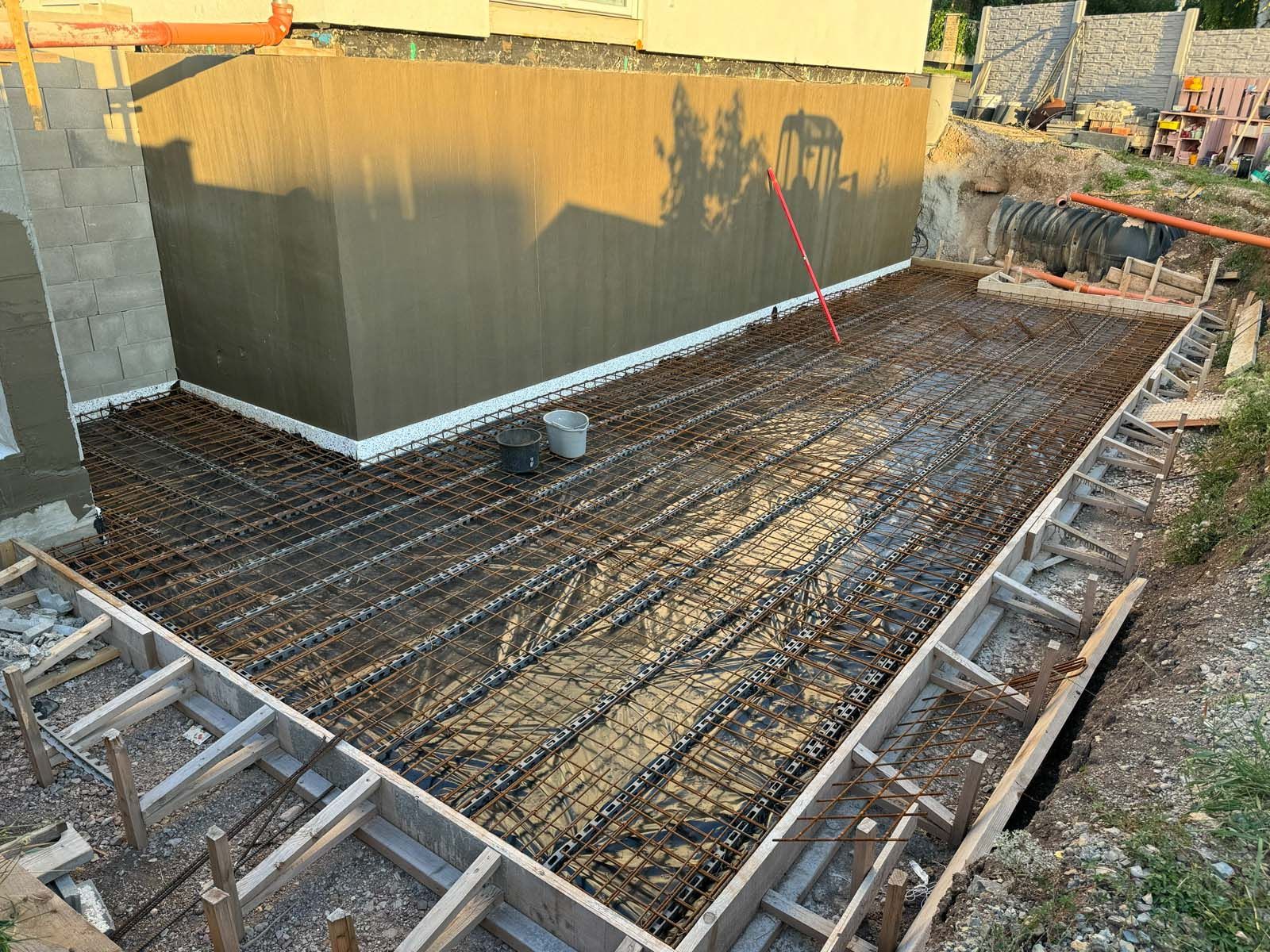 Frisch gegossene Betonplatte neben einem Gebäude, mit Bewehrungsgitter und Holzschalung an den Rändern