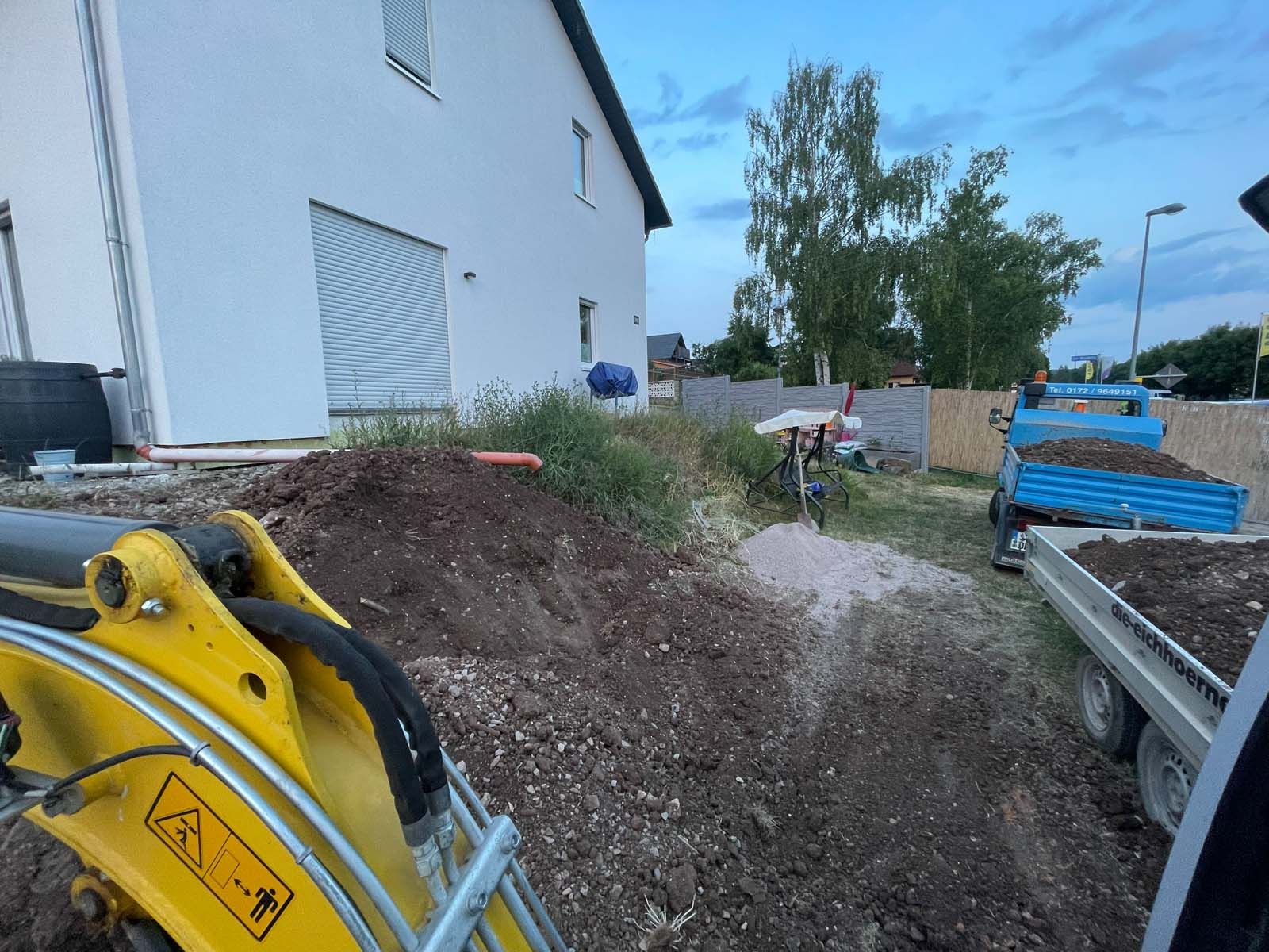 Baustelle neben einem Haus, mit Baggerarm und Haufen von Erde und Baumaterialien