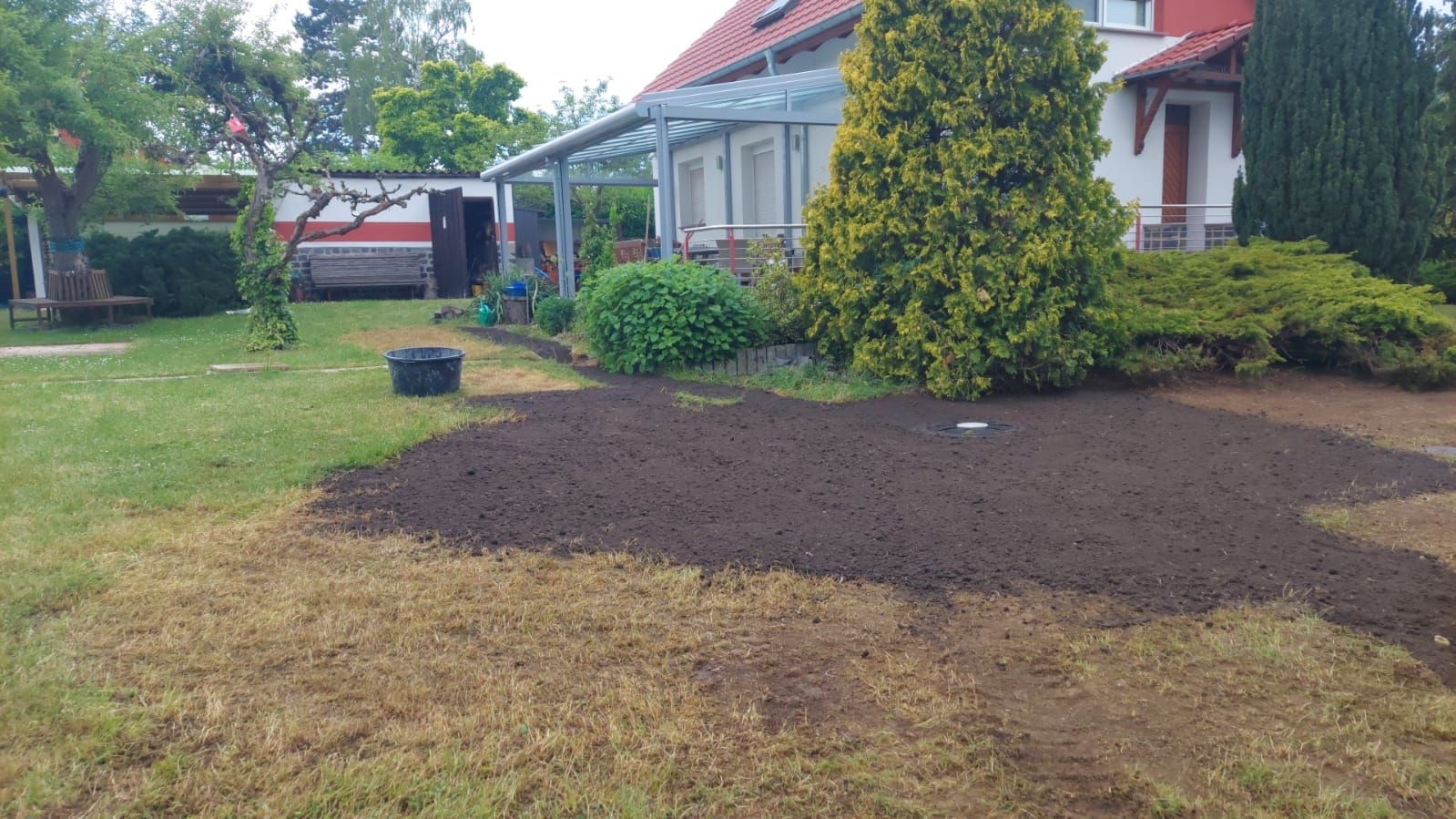 Hinterhof mit einem großen Stück frischer, dunkler Erde neben einem Haus und Sträuchern