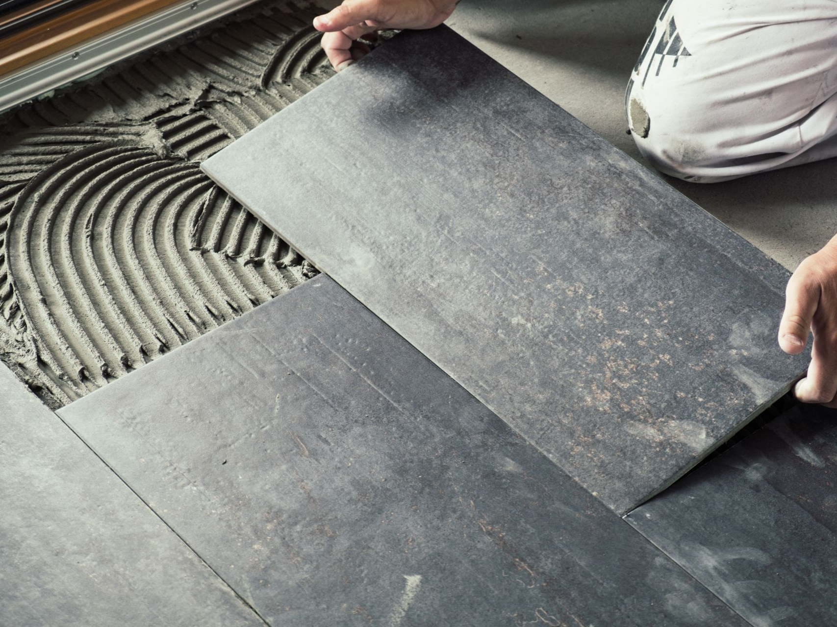Personne posant des carreaux de sol rectangulaires gris foncé avec du ciment.
