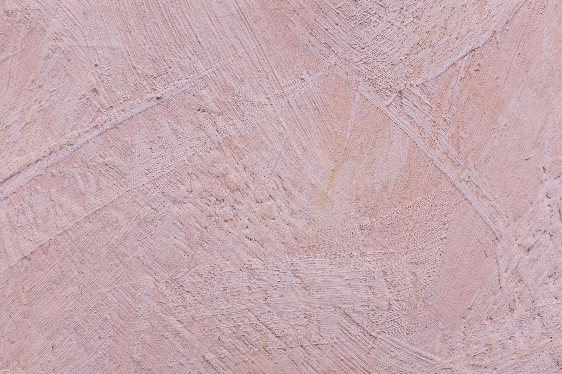 Gros plan sur un mur rose poussiéreux à la finition texturée et grossière, présentant des motifs de coups de pinceau entrecroisés et obliques.