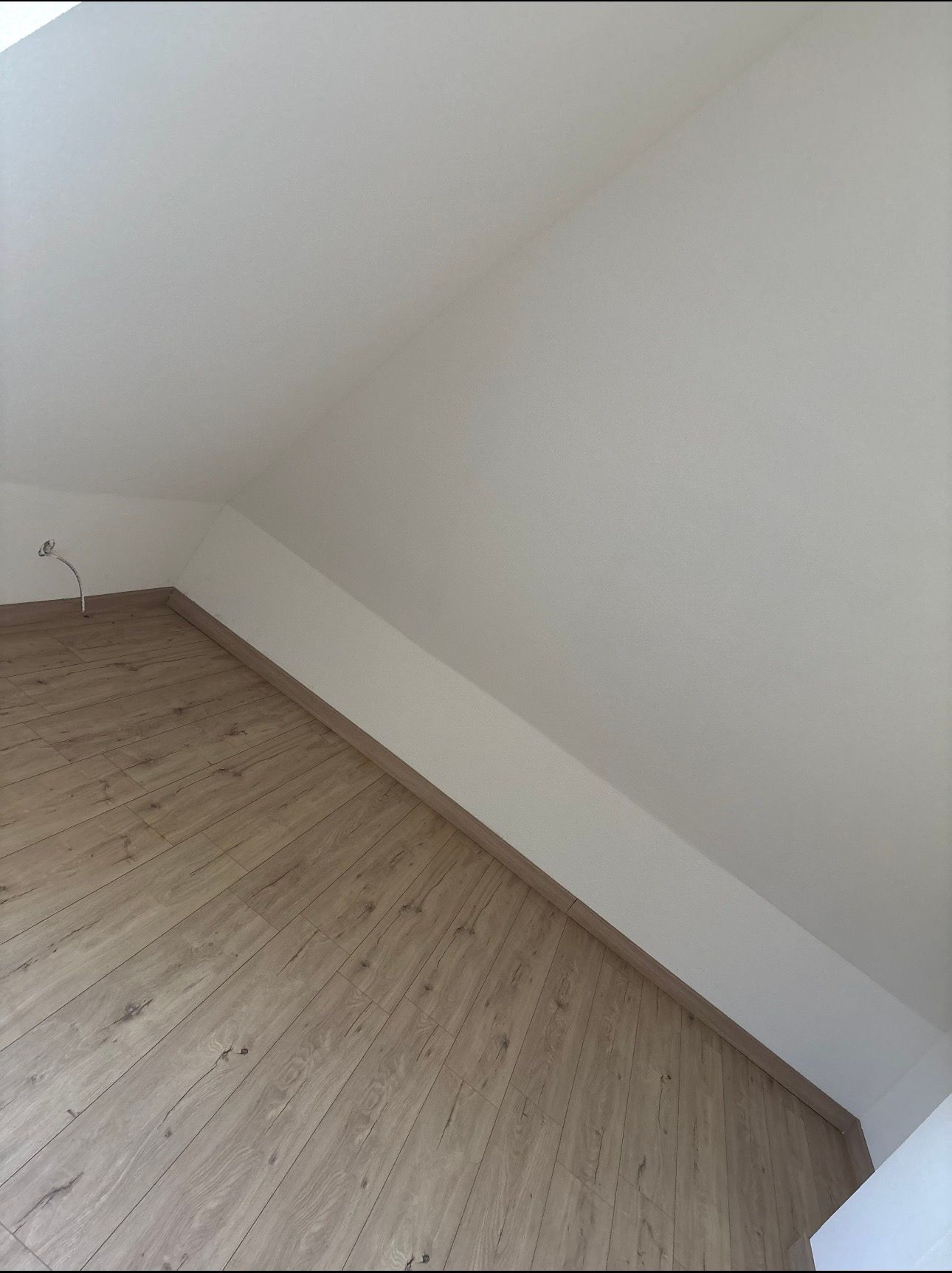 Une pièce mansardée vide avec des plafonds blancs en pente et un parquet clair.