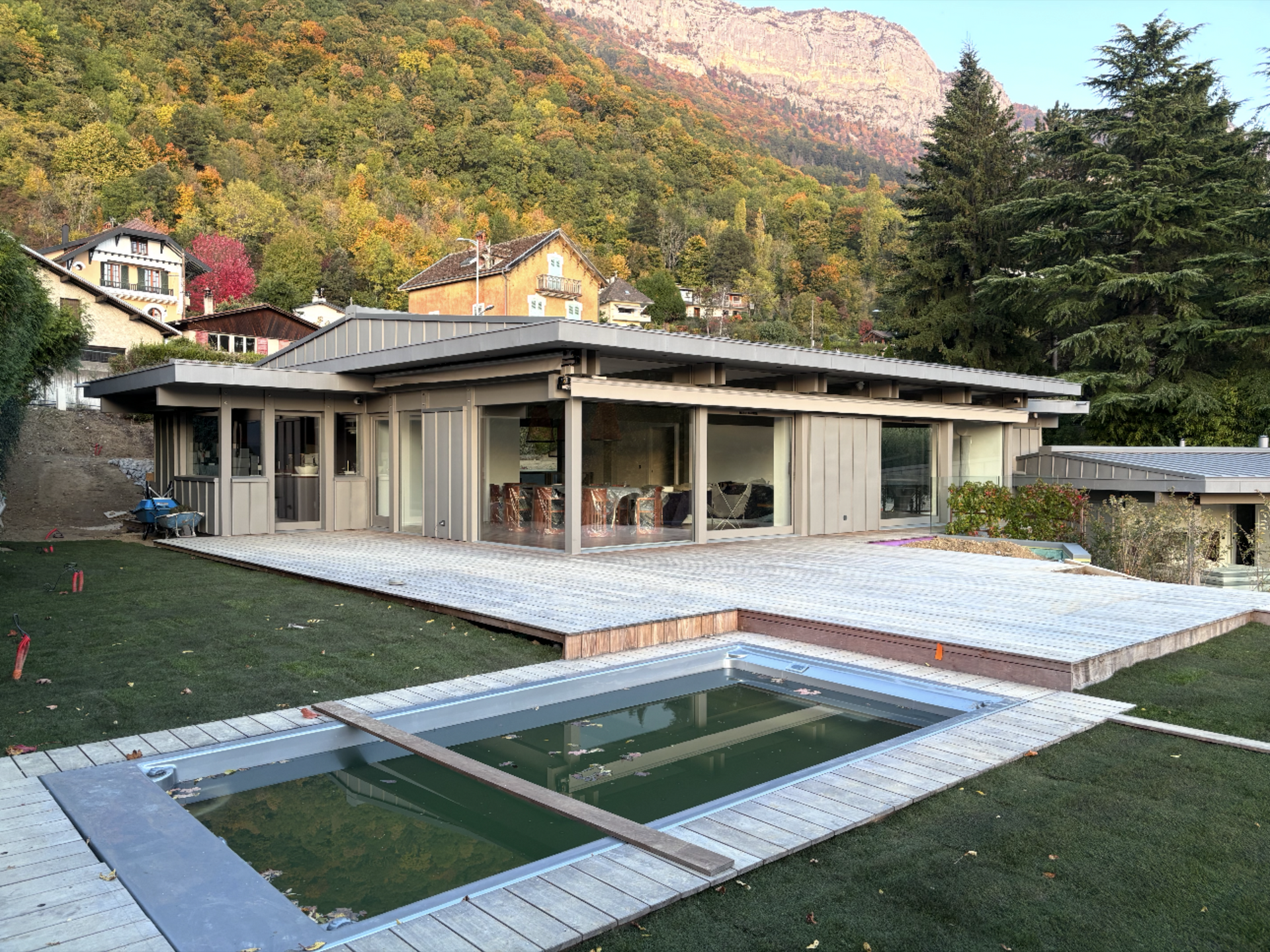 Maison moderne avec piscine et terrasse en bois, avec les montagnes en toile de fond.