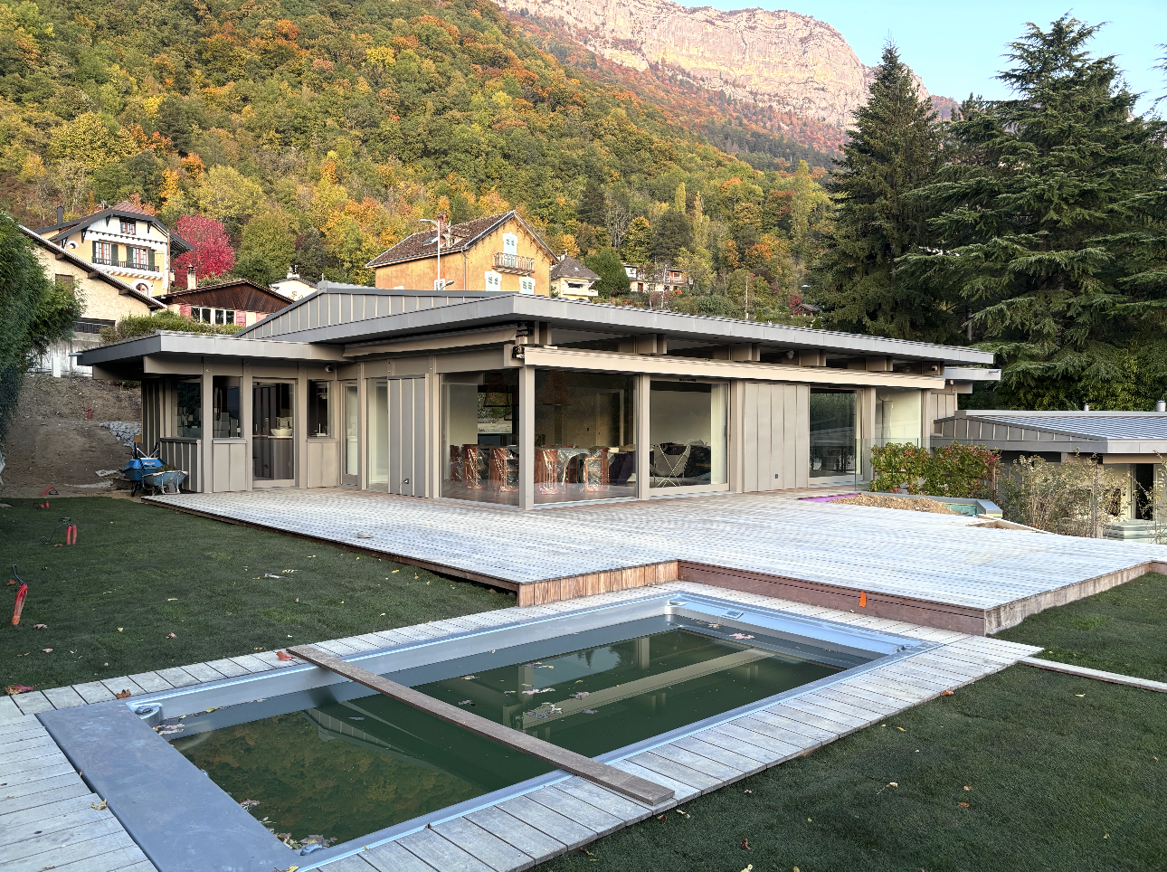 Maison moderne avec piscine et terrasse en bois, avec une montagne et des arbres en toile de fond.