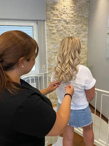 Frau mit lockigem blondem Haar lässt sich ihre Kleidung von einer anderen Frau richten.