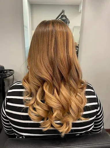 Frau mit braunem bis blondem Ombre-Haar, trägt ein schwarz-weiß gestreiftes Hemd und hat Locken im Haar.