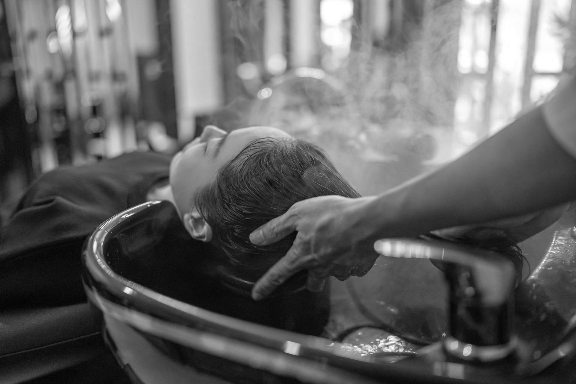 Person lässt sich in einem Salon die Haare waschen. Hände waschen die Haare, während Dampf aufsteigt.