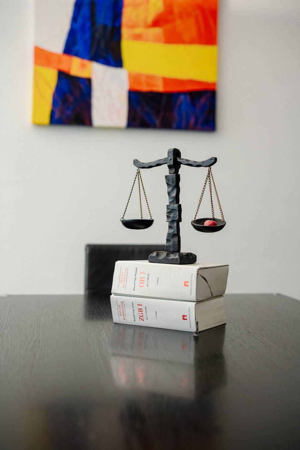 Justitia-Waagen auf Gesetzbüchern, im Hintergrund verschwommene, farbenfrohe Illustrationen.