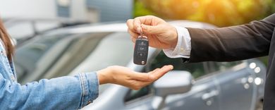 Autoschlüssel werden einer Person neben einem silbernen Auto im Freien überreicht.