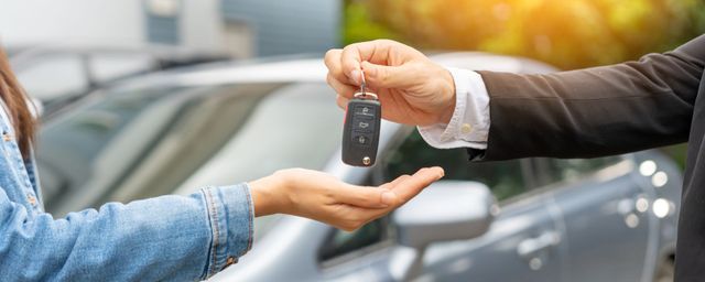 Autoschlüssel werden einer Person neben einem silbernen Auto im Freien überreicht.