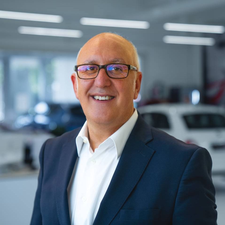 Lächelnder Mann mit Brille und dunkelblauem Anzug in einem hellen Autohaus