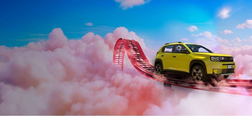 Gelber Geländewagen auf einer roten Rundstrecke über rosa Wolken unter blauem Himmel