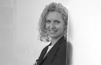 Una mujer con traje está apoyada contra una pared y sonriendo.