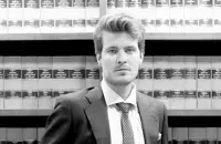 Un hombre con traje y corbata está de pie frente a una estantería.