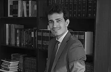 Un hombre con traje y corbata está de pie frente a una estantería.