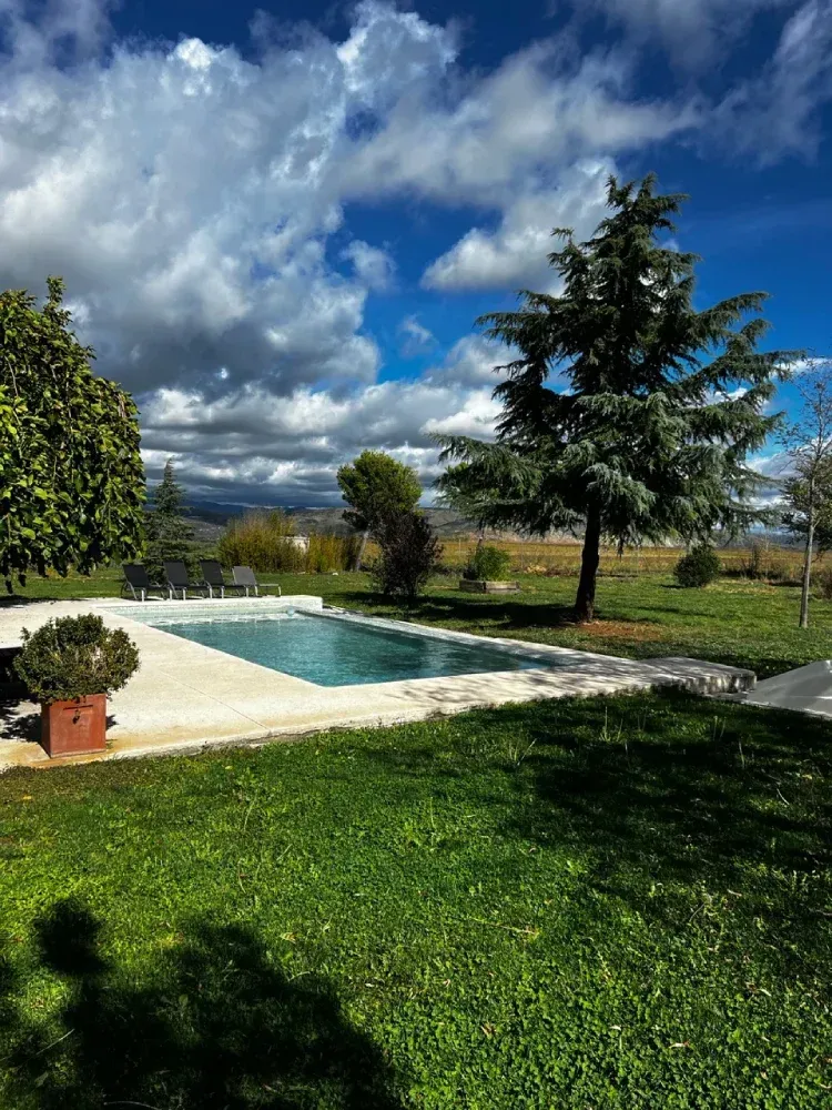 Piscina en un jardín verde bajo un cielo parcialmente nublado con árboles.