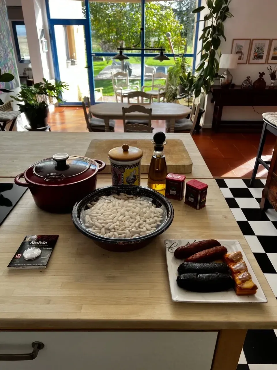 Ingredientes sobre la isla de la cocina: arroz, salchicha, olla, especias, aceite y vistas al jardín.