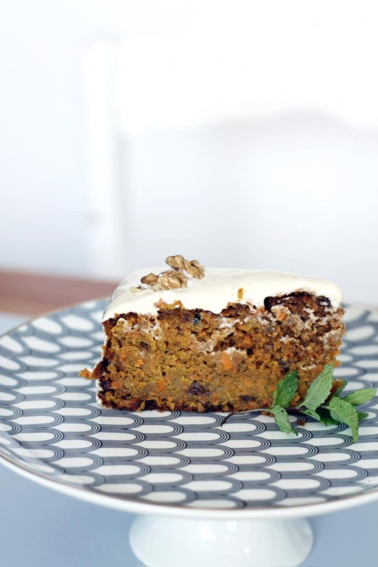 Rebanada de pastel de zanahoria con glaseado blanco y una nuez en un plato decorado.