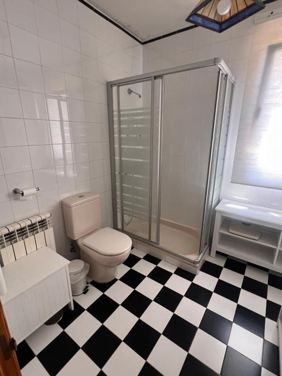 Baño con paredes alicatadas blancas, suelo de baldosas blancas y negras, ducha, inodoro y lavabo.