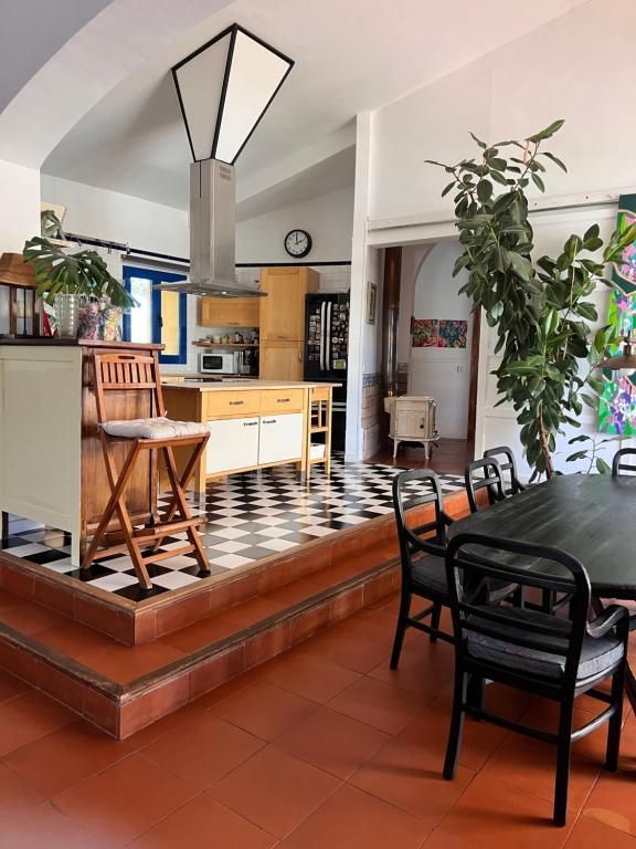 Cocina con suelo de baldosas blancas y negras, armarios de madera y zona de comedor con sillas negras.