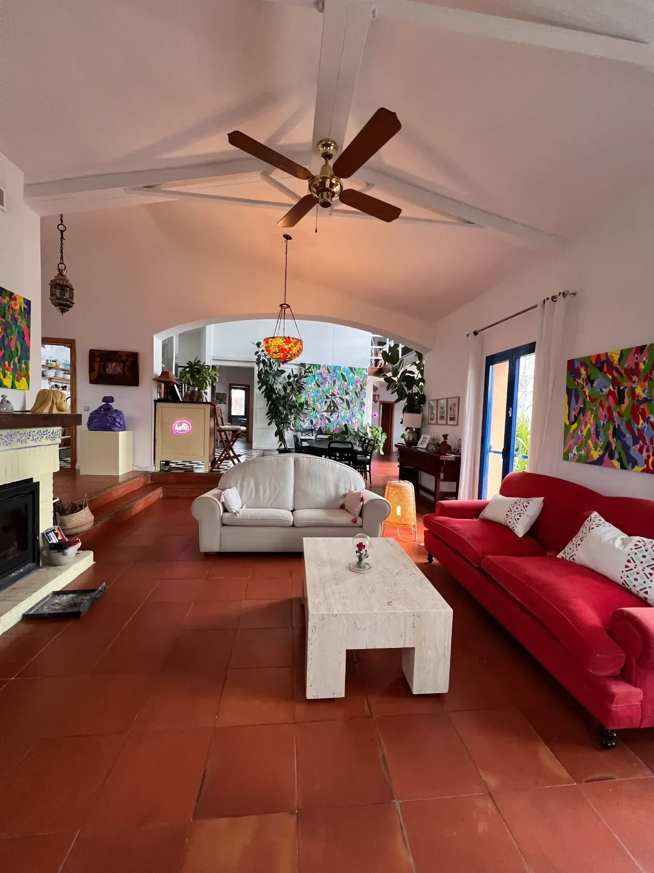 Sala de estar con suelo de baldosas rojas, sofás blancos, sofá rojo, vigas blancas, obras de arte.