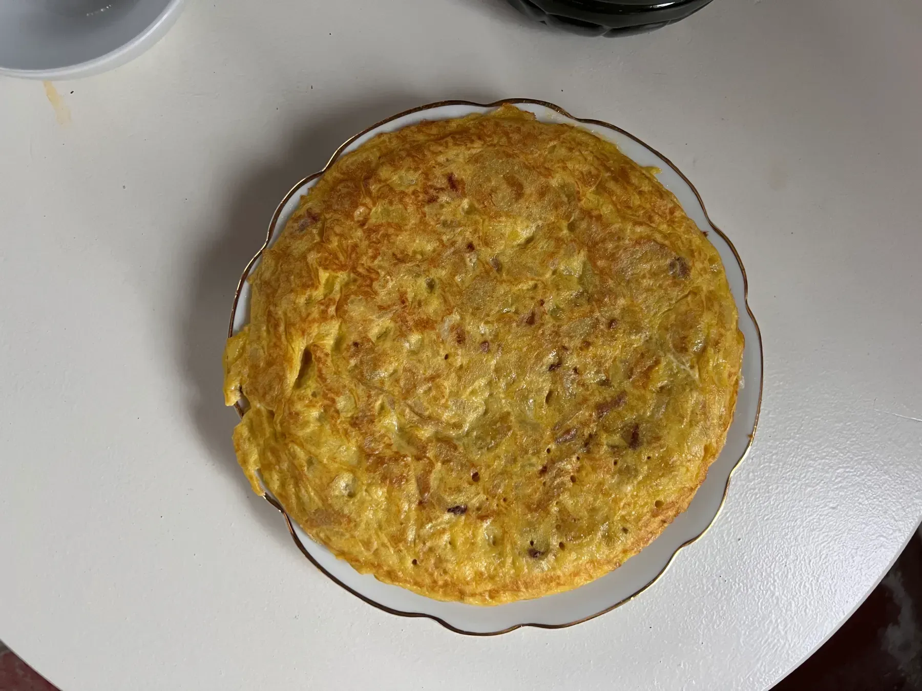 Tortilla Española sobre un plato blanco con borde dorado sobre una superficie blanca.