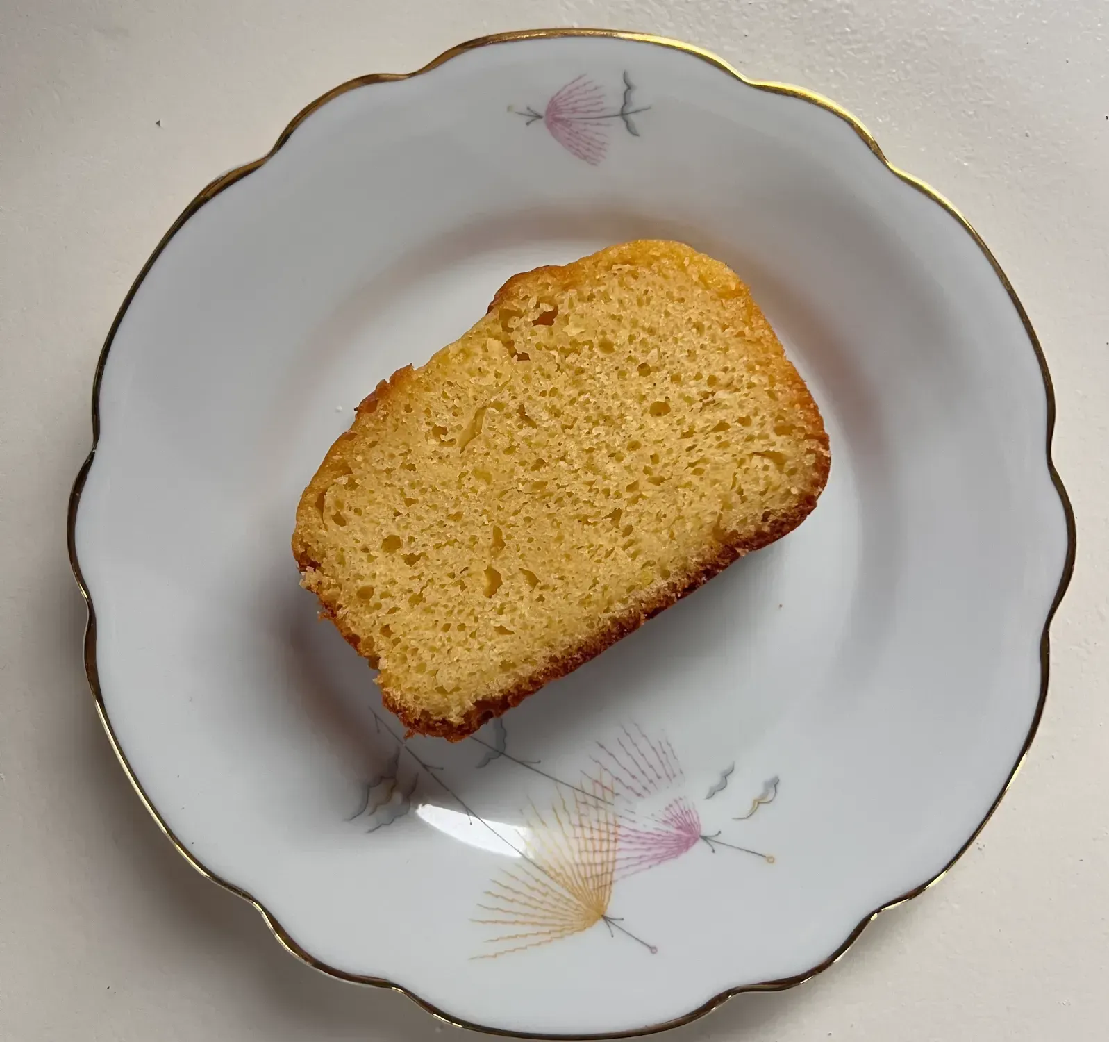 Rebanada de pastel dorado sobre un plato blanco con diseño floral y ribete dorado.