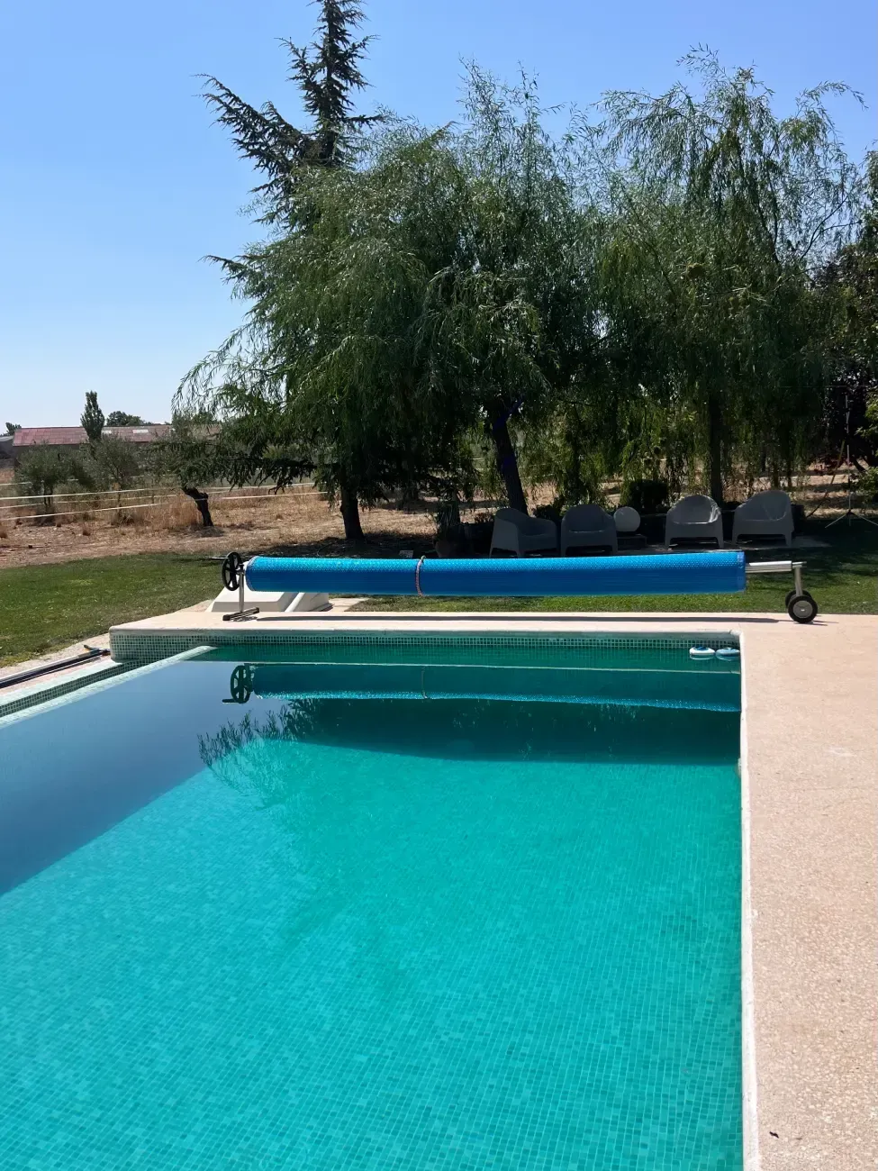 Piscina azul cubierta en un día soleado. Árboles y césped verdes al fondo.