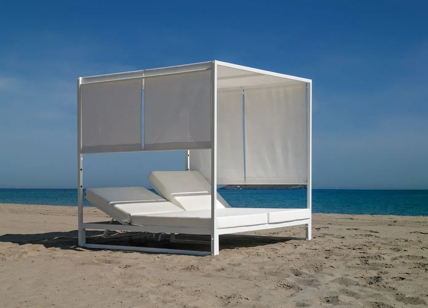 Una cama con dosel se encuentra en una playa de arena cerca del océano.