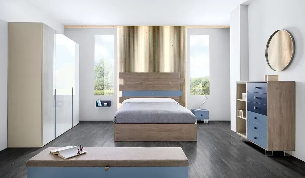 Dormitorio con cama, cómoda, armario, baúl y espejo en tonos neutros y azules.
