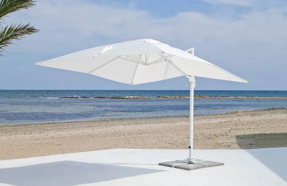 Una sombrilla blanca está sentada en un patio blanco al lado de una playa.