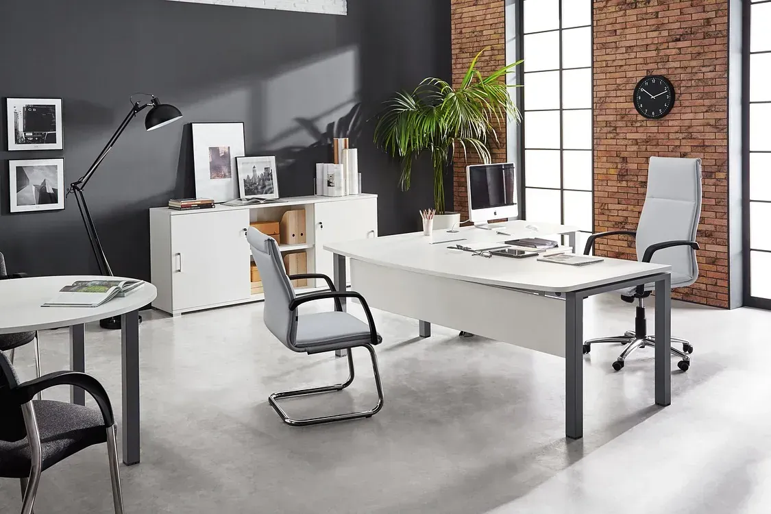 Una habitación con un escritorio, sillas, armarios y un reloj en la pared.