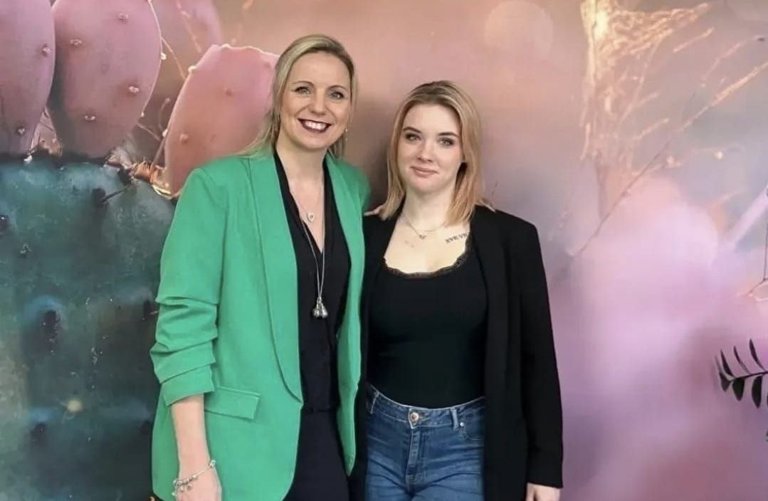 Vier Frauen posieren für ein Foto vor einer Wand mit Blumen darauf.