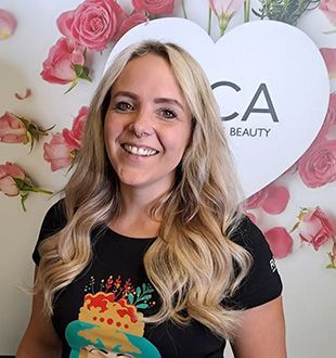 Jacqueline Lechner - Team von Dream Hair aus Pulheim Eine Frau lächelt vor einem Herz mit Rosen darauf.