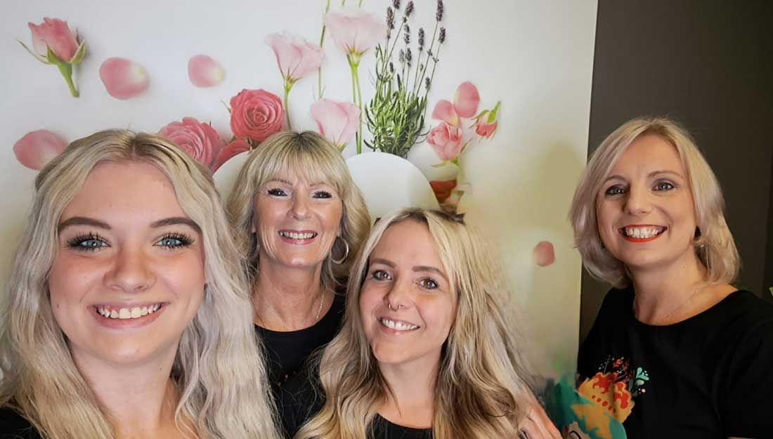 Das Team von Dream Hair aus Pulheim Vier Frauen posieren für ein Foto vor einer Wand mit Blumen darauf.