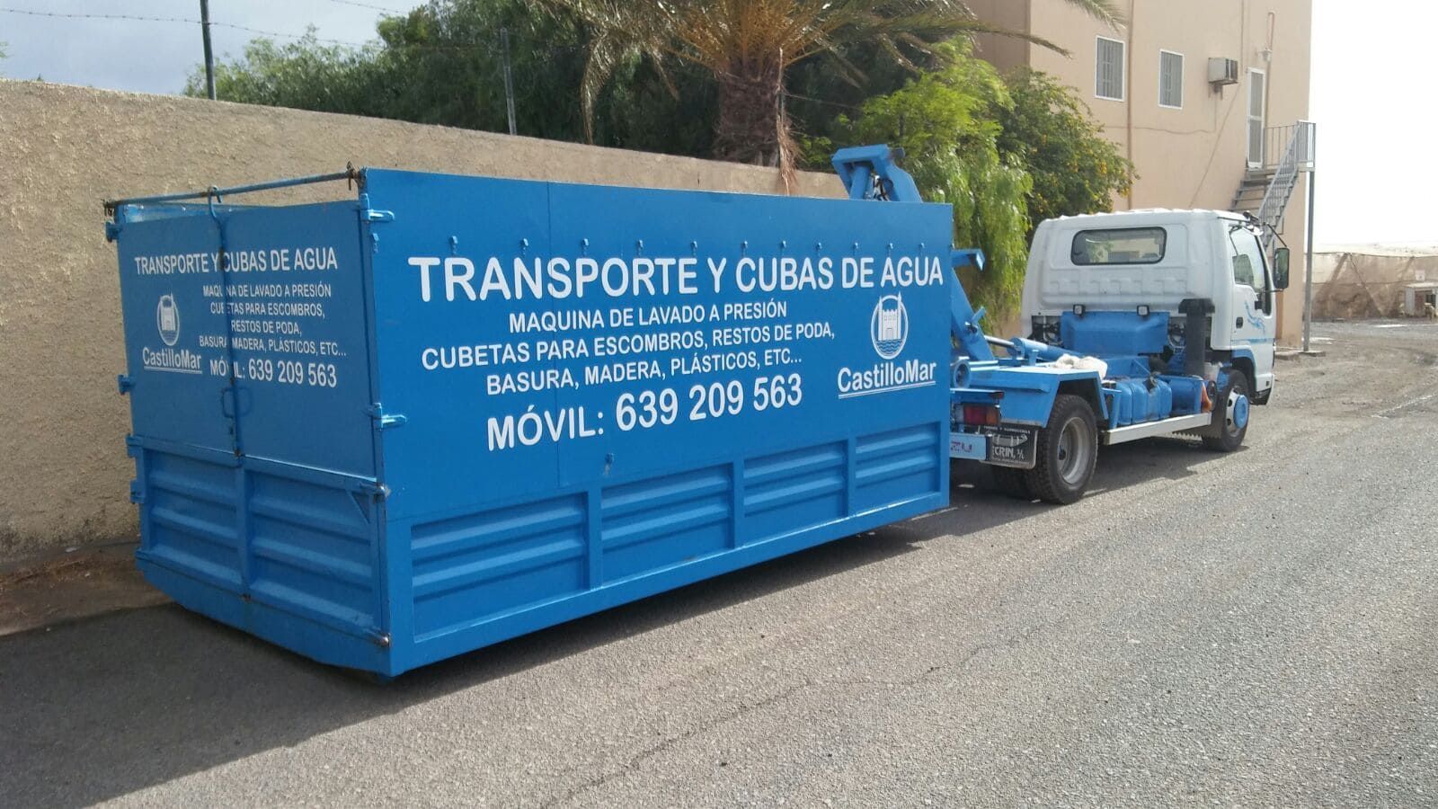 Un contenedor de basura azul está estacionado al lado de un camión blanco.
