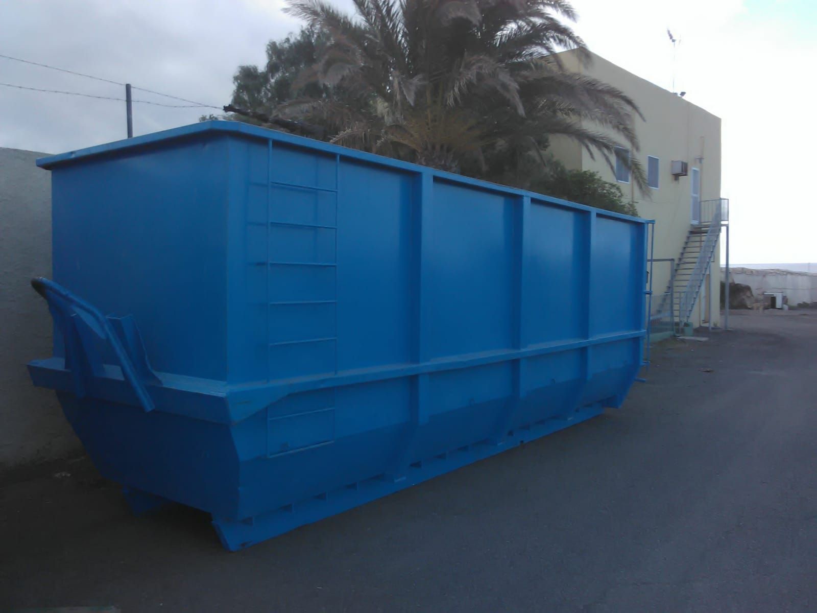 Un gran contenedor de basura azul está estacionado frente a un edificio.