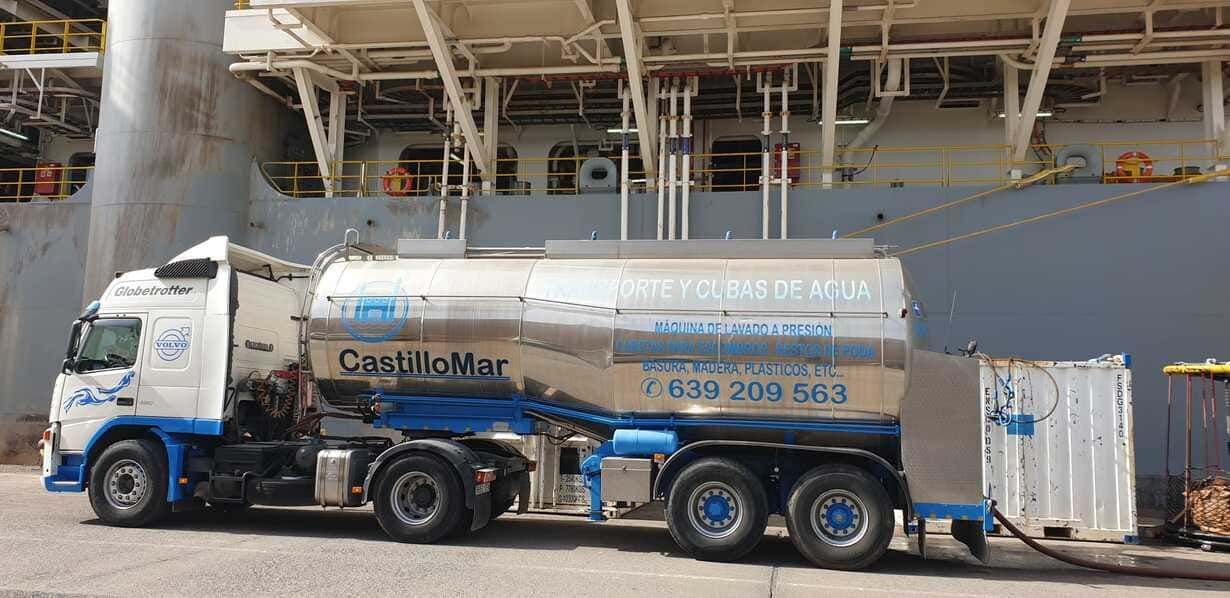 Un camión blanco y azul está estacionado frente a un gran barco.