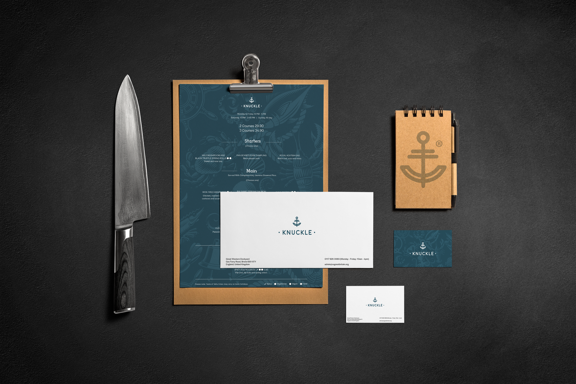 A chef's knife, a menu on a clipboard, a notepad with an anchor icon, and business cards on a dark, textured background.