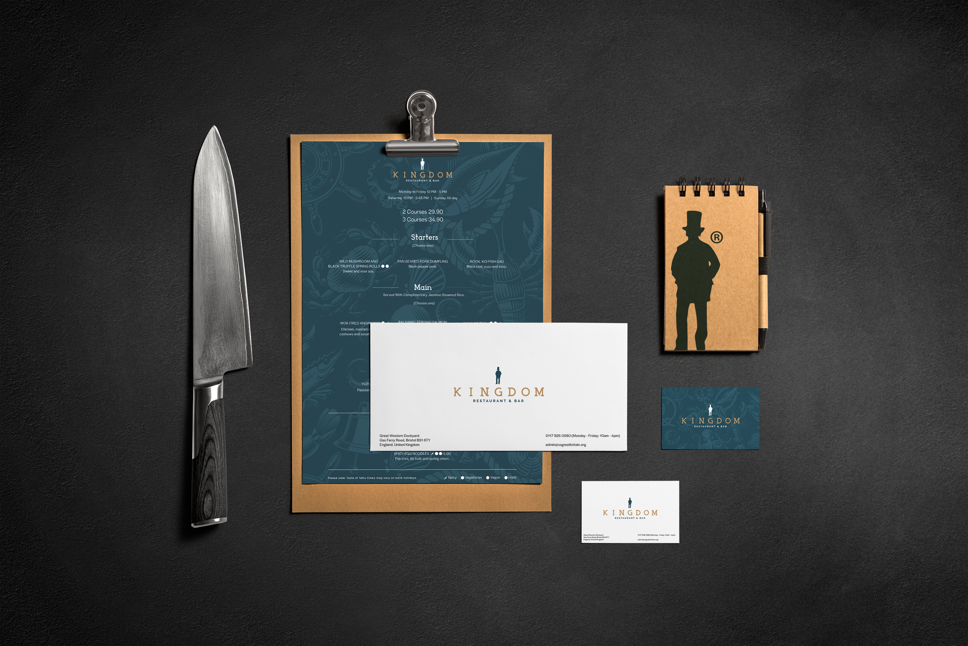A branding set featuring a knife, menu, notepad, and business cards on a dark, textured background.