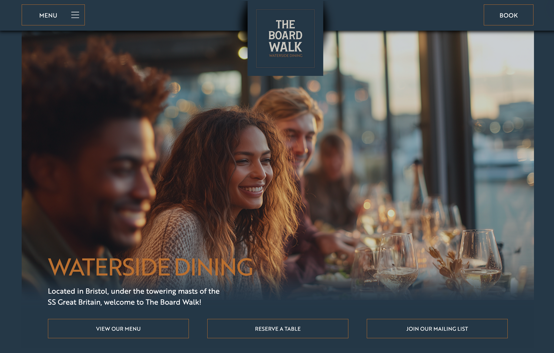 A diverse group of people dining together at a restaurant overlooking a harbor at sunset.