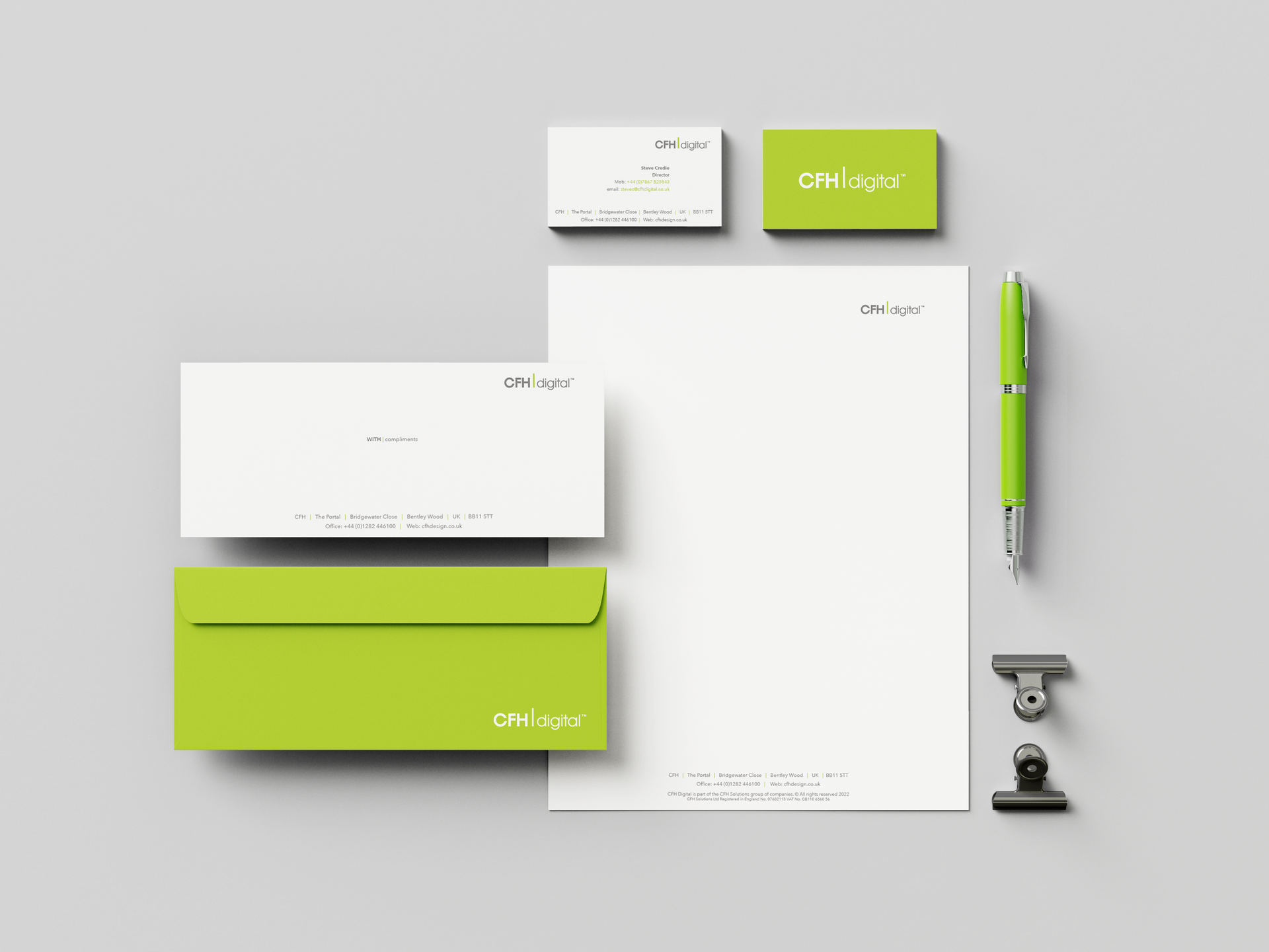 A corporate stationery set including a letterhead, business cards, envelopes, a lime green pen, and clips on a gray surface.