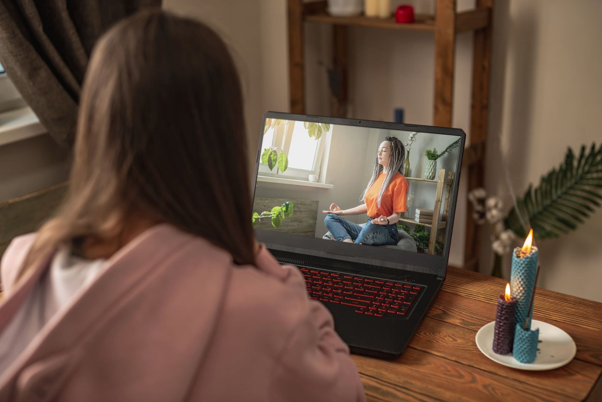 Una mujer está sentada frente a una computadora portátil mirando un vídeo de una mujer meditando.