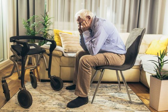 Un anciano está sentado en una silla en una sala de estar al lado de un andador.