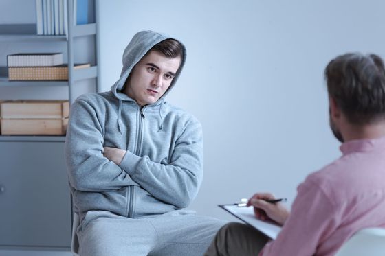 Un joven está sentado en una silla hablando con un hombre que sostiene un portapapeles.