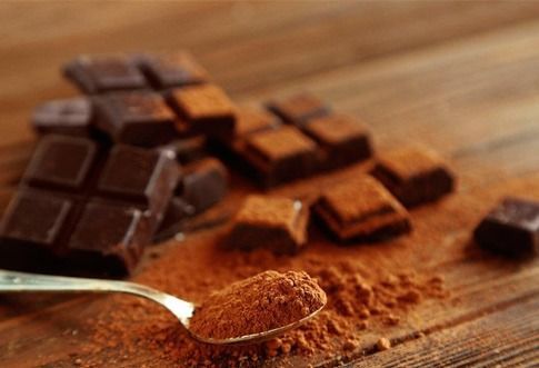 Una cucharada de cacao en polvo está sobre una mesa de madera al lado de una barra de chocolate.